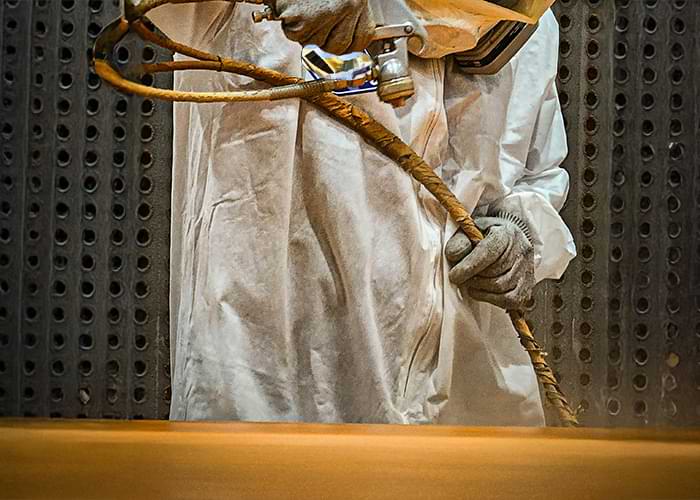 Worker in a protective suite using a compressed air paint sprayer